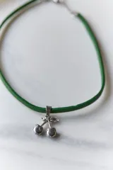 Gargantilla con cordón rojo y dije de cerezas rojas con detalles dorados y hojas verdes.