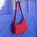 Cartera negra ovalada de simil cuero con cierre y correa ajustable con ojales. Cuenta con bolsillos internos y un bolsillo trasero.