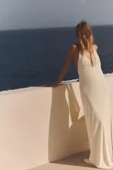 Vestido largo color blanco con cuello halter y escote en pico pronunciado. Detalle de frunces, forro interior y abertura en la espalda.