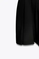 Vestido corto negro sin mangas, con cuello redondo y falda con tablas. Cierre trasero con cremallera oculta.