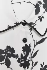 Camisa blanca con estampado floral negro, cuello solapa, manga larga y cierre frontal con botones.