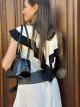 Vestido midi color crudo con detalles en negro en cuello, volados y ruedo. Incluye cinturón ancho negro con tachas y hebilla dorada.