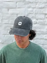 Gorro tipo gorra de béisbol color gris oscuro con efecto lavado, con un pequeño logo bordado en blanco en el frente.