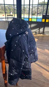 Campera puffer negra con estampado de flores y aves, capucha con borde de piel sintética marrón, bolsillos laterales y forro de algodón.