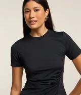 Blusa negra ajustada de microfibra con cuello redondo y mangas cortas. Presenta fruncido en el lateral y encaje en el bajo.