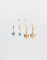 Set de tres pares de aros dorados: un par de aros tipo argolla con dije de corazón labrado, un par de aros tipo argolla con dije de cerámica estampada en azul y blanco, y un par de aros tipo botón con perlas sintéticas.