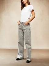 Jean de mujer color gris claro lavado, tiro alto, corte ancho y recto (wide leg). Presenta costuras marcadas en el frente de las piernas con pequeños detalles metálicos o tachas a lo largo de la costura.