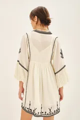 Vestido corto negro con bordado de hilo blanco, escote en V y mangas largas abullonadas.