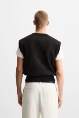 Chaleco negro de punto con cuello en V, corte cropped y sisas amplias. Tejido en hilatura de algodón con acabados en rib.