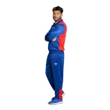 Conjunto deportivo azul con detalles en rojo y blanco, compuesto por campera con cierre y pantalón largo. La campera tiene cuello alto, cierre frontal, bolsillos laterales, puños y cintura elastizados, y el logo de Umbro y el escudo del Club Nacional de Football bordados en el pecho. El pantalón tiene cintura elástica con cordón ajustable, bolsillos laterales y el logo de Umbro bordado en la pierna.