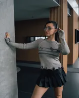 Sweater gris de punto con rayas verticales negras, cuello redondo, mangas largas con detalle de flecos y ruedo con terminación irregular.