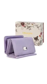 Billetera corta de símil cuero color beige claro, con cierre de broche a presión en la solapa principal. Presenta múltiples compartimentos internos para tarjetas y billetes, y un bolsillo exterior con cierre en la parte posterior. Lleva una placa metálica con el logo de la marca.