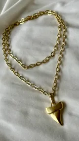 Collar dorado de doble cadena con dije de diente de tiburón.