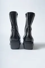 Bota corta negra de cuero con caña ajustada, punta cuadrada y taco ancho y bajo. Presenta un cierre lateral y costuras visibles en el empeine.