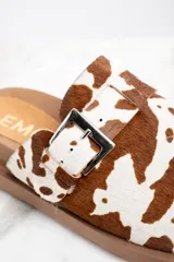 Zuecos con capellada de cuero con estampado animal print de vaca, base marrón con suela track y hebilla metálica ajustable.