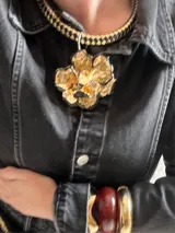 Collar corto con cadena gruesa tejida en dorado y negro, con dije grande de flor dorada texturizada.
