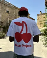 Remera blanca de algodón con corte oversize y estampado grande en la espalda de dos cerezas rojas unidas por el tallo, con el texto "Nude® Project" debajo.