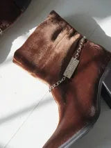 Bota corta de velvet azul marino con efecto abullonado en el tobillo y cierre lateral con cremallera. Tiene un tacón cuadrado y una cadena desmontable con el logo de la marca.