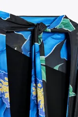 Vestido largo de tejido fluido con estampado floral azul sobre fondo negro. Tiene cuello subido con frunces y lazada, espalda descubierta, forro interior y abertura lateral en el bajo.