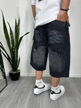 Bermuda de jean negro con diseño baggy, largo hasta la rodilla, con roturas y estampado de calaveras en los bolsillos traseros.