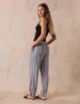 Pantalón largo de lino y rayón a rayas verticales grises y blancas. Tiene pretina elastizada con lazo de ajuste, bolsillos delanteros y traseros.