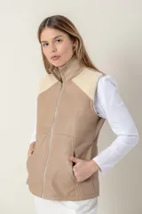 Chaleco de cuero color beige con cuello alto, cierre frontal y bolsillos laterales. Presenta apliques de piel sintética color crema en los hombros.