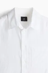 Camisa blanca de lino y algodón con cuello inglés, tapeta clásica y canesú en la espalda. Modelo de manga larga con bolsillo superior abierto, cierre ajustable de botón en los puños y tapeta con botón. Bajo redondeado. Corte estándar.