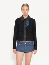Chaqueta corta negra de gabardina combinada con cuero, con recortes delanteros, bolsillos plaqué con tapa y broches forrados. Presenta volados en denim.
