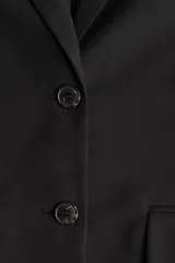 Blazer negro de sarga con solapas de muesca, hombreras, bolsillos ribeteados con solapa y forro interno.