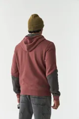 Campera marrón de felpa con capucha, cierre frontal y bolsillos laterales con cierre. Presenta mangas largas negras y logo de la marca estampado en el pecho.