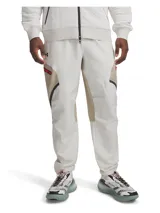 Pantalón cargo Under Armour Unstoppable para hombre, color beige con paneles laterales en marrón claro y detalles en rojo. Confeccionado en tejido técnico resistente al agua, elástico y duradero. Cuenta con bolsillos cargo con cierre y cintura elástica ajustable.