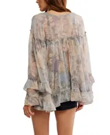 Blusa de chiffon con estampado floral en tonos pastel y grisáceos. Presenta escote en V con cierre frontal de botones nacarados, mangas largas amplias con puños con volados y un ruedo con volado en el bajo.