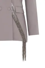 Blazer gris de corte estructurado con doble abotonadura y solapas clásicas. Presenta una aplicación de pedrería en cascada que recorre diagonalmente la prenda.