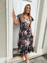 Vestido midi negro con estampado abstracto en tonos beige y blanco, mangas cortas con volados y falda con volados en el ruedo.