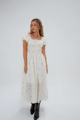 Vestido midi blanco con estampado floral celeste, escote cuadrado con detalle de lazo, mangas cortas abullonadas y falda con volados.