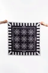 Pañuelo o bandana cuadrado de tela fina, color negro y blanco, con borde de franjas verticales blancas y negras. El centro negro presenta un patrón de nueve figuras estilizadas que parecen personas tomadas de la mano formando una flor o estrella.