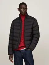Campera acolchada negra de nailon con aislamiento térmico y acabado repelente al agua. Tiene cuello alto, cierre de cremallera, dos bolsillos delanteros y parche engomado del logo de Tommy Hilfiger en la manga.
