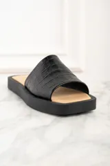 Sandalia abierta negra con textura de cuero de cocodrilo y suela plana.