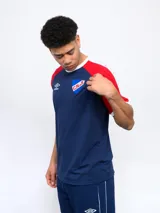 Remera de algodón azul con mangas ranglan azul marino y detalles en blanco en cuello y puños. Incluye logo de Umbro y escudo del Club Nacional de Football en el frente.