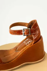 Sandalias de cuero color marrón con plataforma y taco de cuña. Tiras anchas con textura tipo cocodrilo y hebilla metálica plateada.