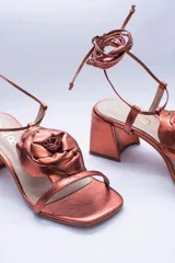 Sandalias de cuero color champagne, con taco cuadrado, tira delgada sobre los dedos y tobilleras para atar. Presentan un aplique de flor de cuero en la capellada.