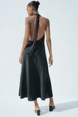 Vestido midi negro de tejido fluido, con cuello halter que se anuda en la nuca y escote pronunciado en pico.