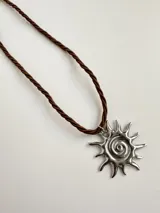 Collar con dije de sol plateado y cordón marrón trenzado.