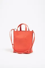Bolso de mano mediano marca Bimba y Lola, color naranja, confeccionado en cuero con textura granulada. Tiene doble asa corta, correa bandolera ajustable y extraíble, logo estampado en el frente y herrajes plateados. El interior cuenta con etiqueta de tejido con el logo de la marca.