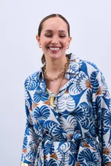 Vestido estilo camisola con estampado floral en tonos azules y marrones, con cuello camisero, mangas largas con puños y cierre frontal con botones. Incluye cinturón de la misma tela.
