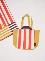Bolso tipo tote XL con diseño a rayas rojas y blancas en el centro y laterales color mostaza. Tiene cierre lateral y manijas cortas color mostaza.