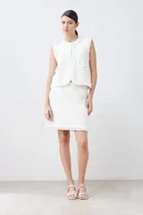 Falda corta color crudo tejida con textura acanalada horizontal y terminación desflecada en el ruedo.