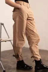 Pantalón de gabardina elástica color beige, estilo cargo/bombacha de gaucho, con bolsillos grandes y tobillos ajustables con tiras de cuero gamuzado.