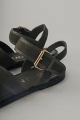Sandalia plana de cuero color verde militar, con tiras cruzadas en el empeine y una tira ajustable con hebilla metálica dorada en el tobillo.