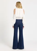 Pantalón de denim azul oscuro, corte acampanado, tiro alto, pretina con trabillas, cierre de botón y cremallera, cuatro bolsillos, ribete vertical y pespuntes.